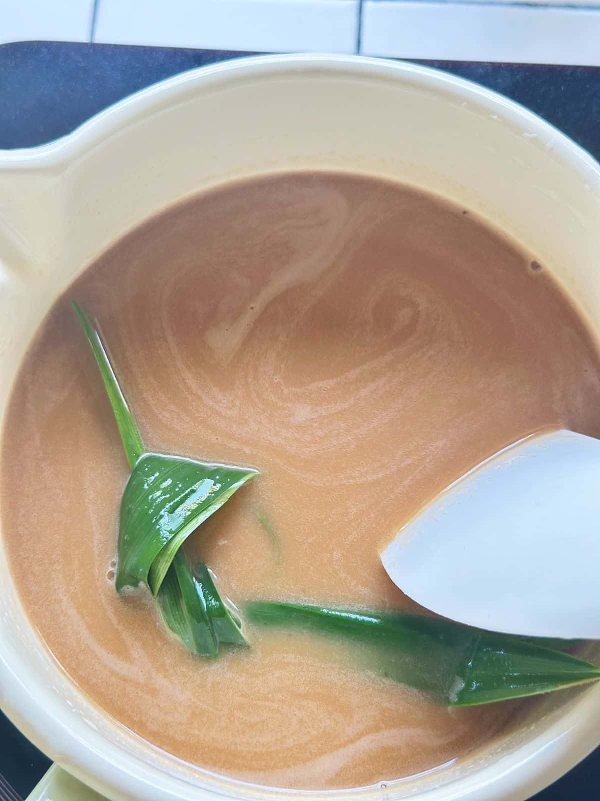 Palm sugar, egg and coconut milk mixture cooking on low heat with pandan leaves.