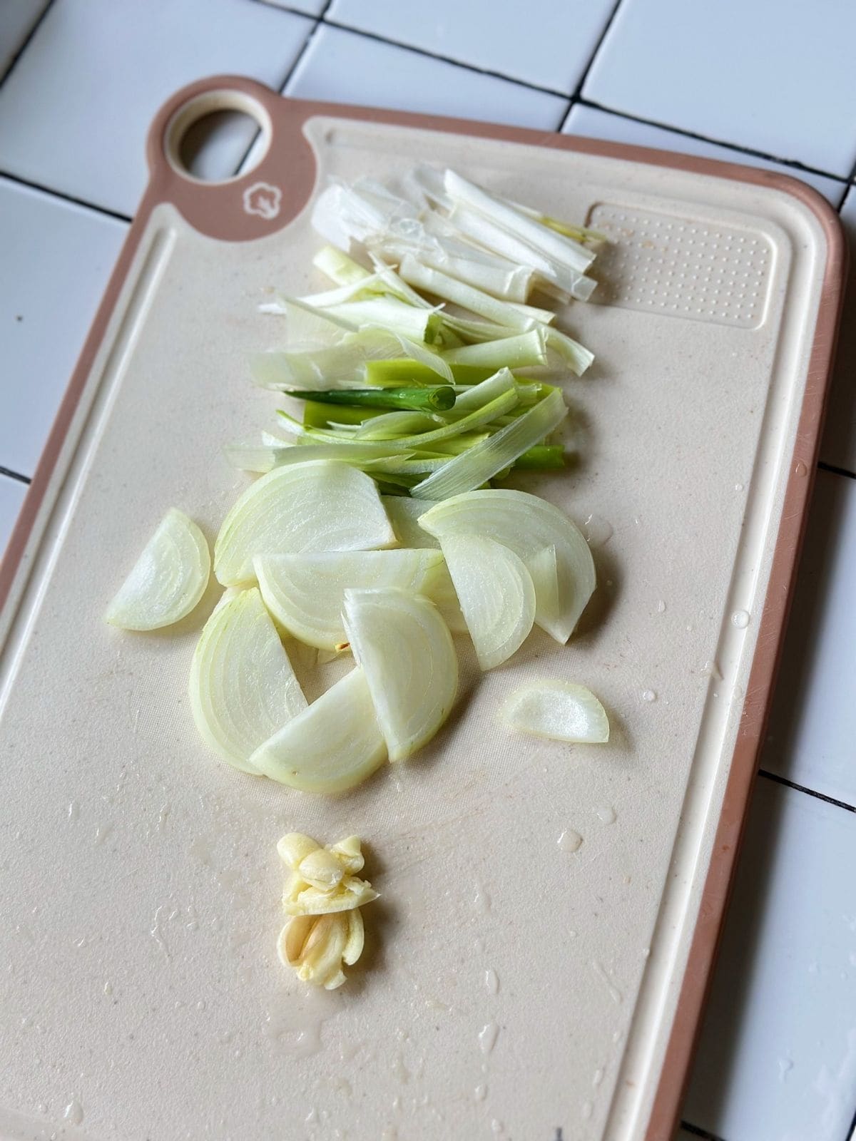 Chopped onion, sliced leeks, and minced garlic arranged on a cutting board, ready for cooking tteokbokki.