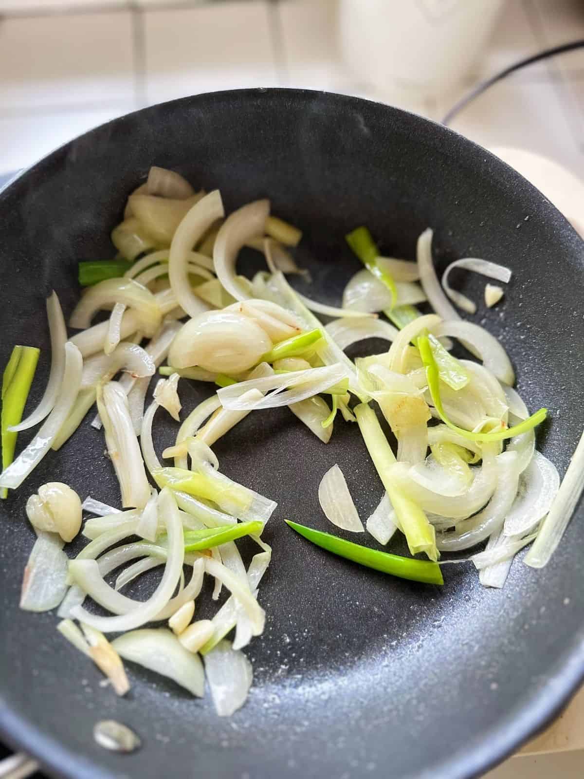 Onion slices and leeks sautéing in a pan until fragrant, the flavor base for tteokbokki sauce.