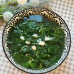 A steaming bowl of Canh Rau Den, Vietnamese amaranth soup, with tender green and red amaranth leaves floating in a clear broth, served simply in a patterned bowl.