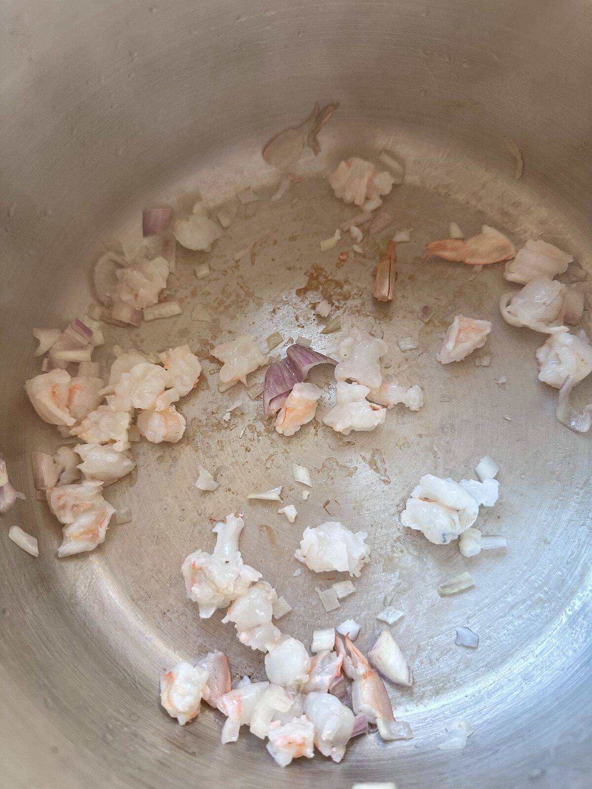 Chopped shrimp and shallots being stir-fried in a pot until fragrant.