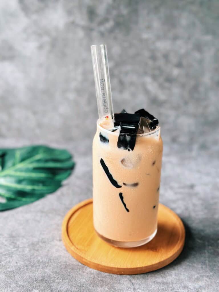 Glass of Vietnamese milk tea served over ice with cubes of grass jelly.