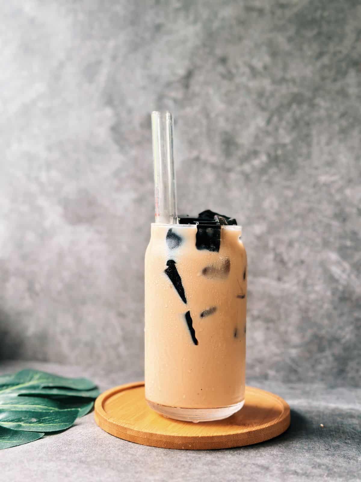 Glass of Vietnamese milk tea served over ice with cubes of grass jelly.