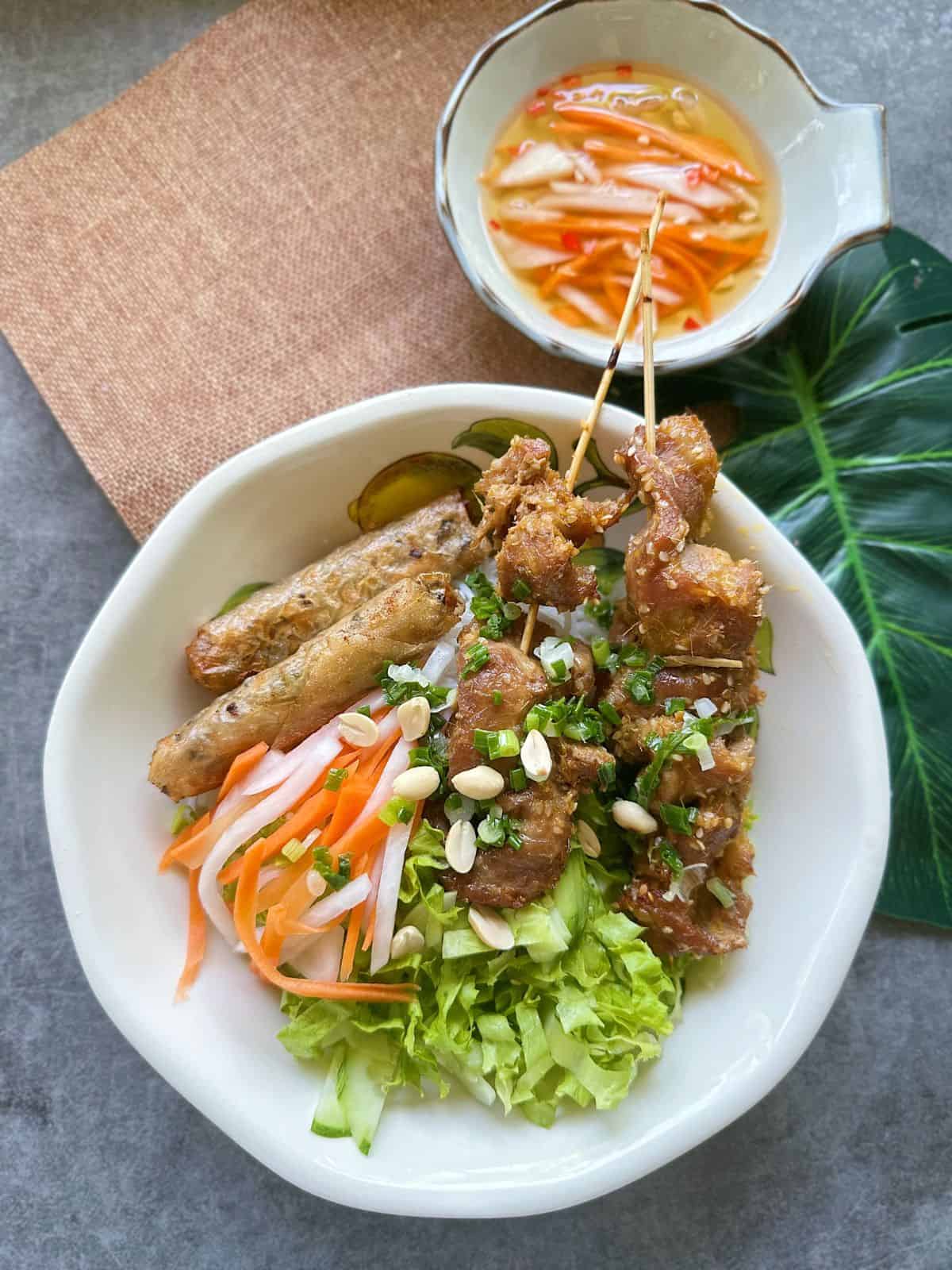 Vietnamese rice noodle bowl with grilled pork skewers, fresh herbs, pickled vegetables, and dipping sauce
