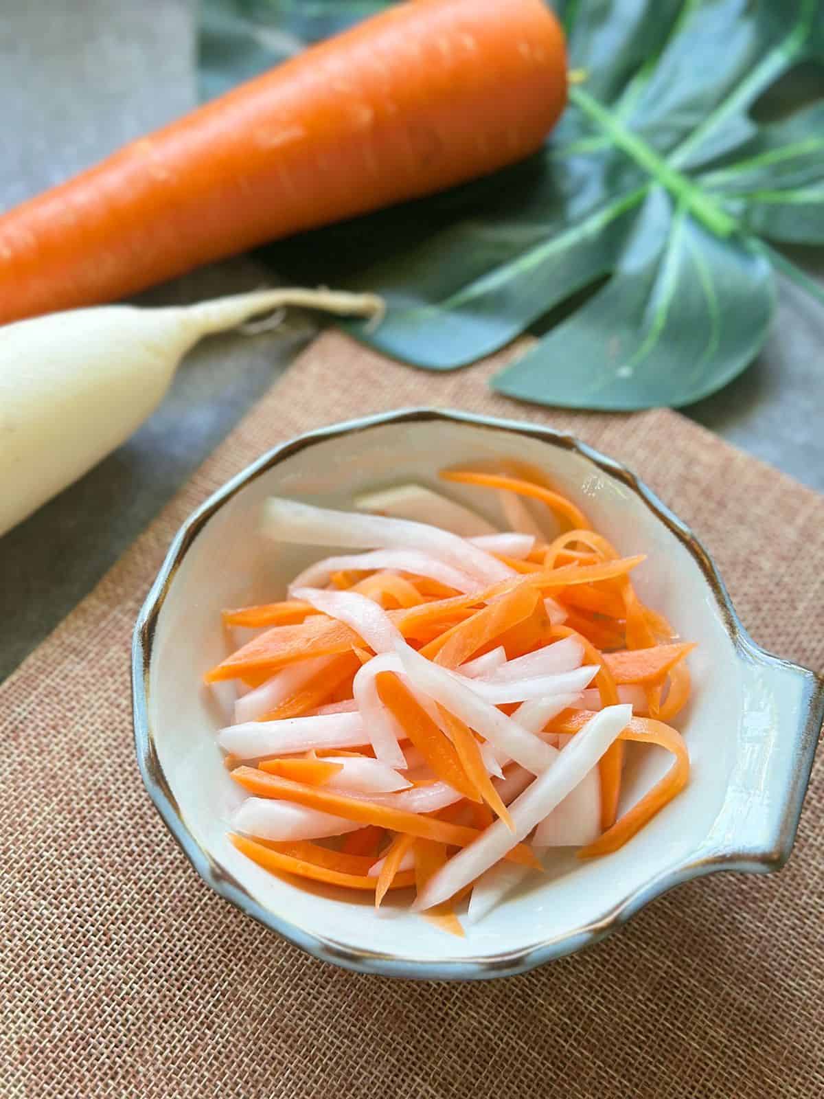 Close-up of Đồ Chua, thinly sliced pickled carrots and daikon in a small white bowl.