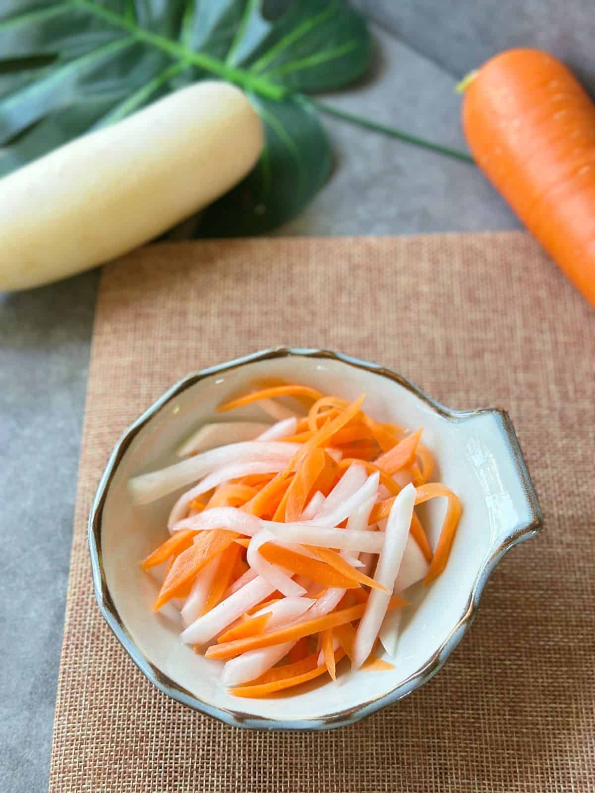 Original Nước Chấm - Vietnamesische Fischsauce Close-up of Đồ Chua, thinly sliced pickled carrots and daikon in a small white bowl.