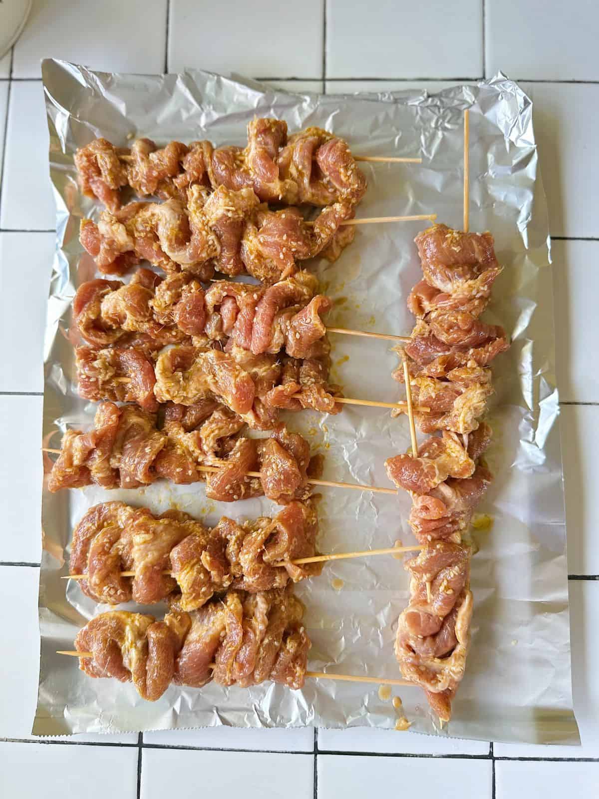 Uncooked Vietnamese pork skewers (Thịt Nướng) arranged on a baking tray before cooking