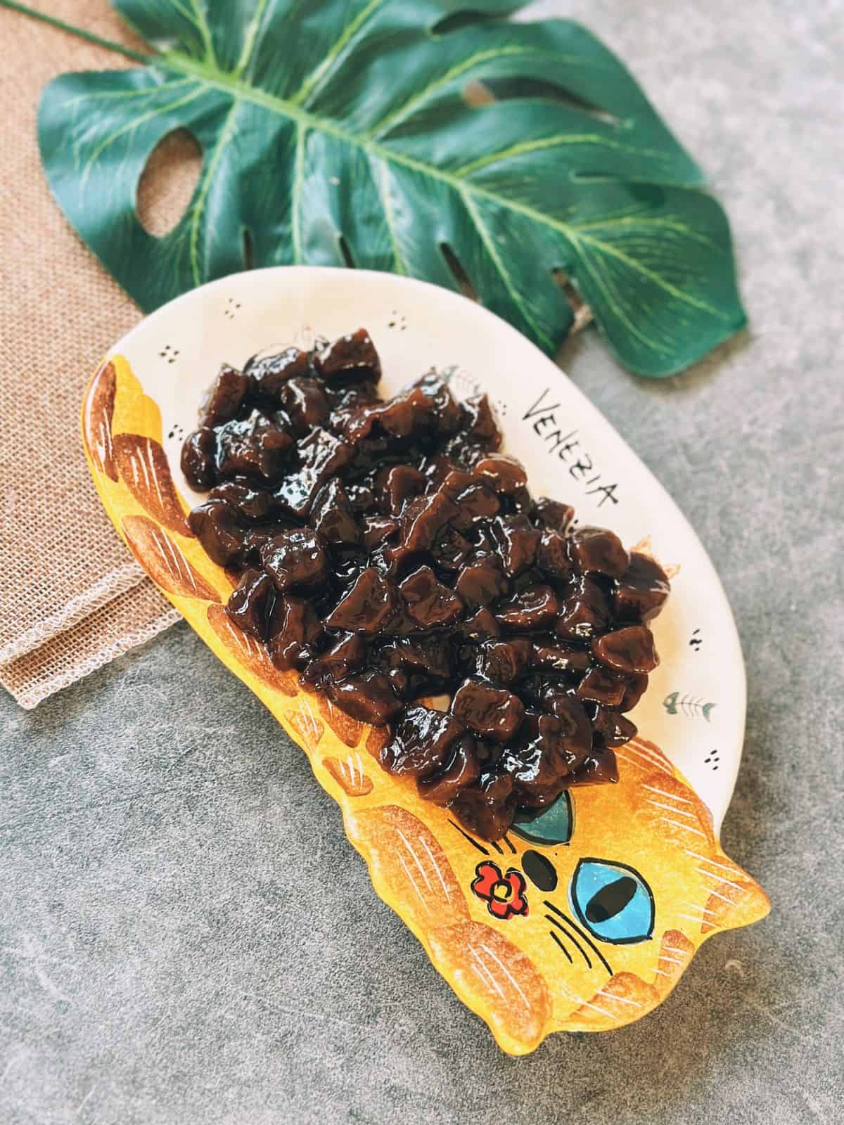 A plate of glossy, cooked boba pearls coated in syrup, glistening and ready to add to milk tea.