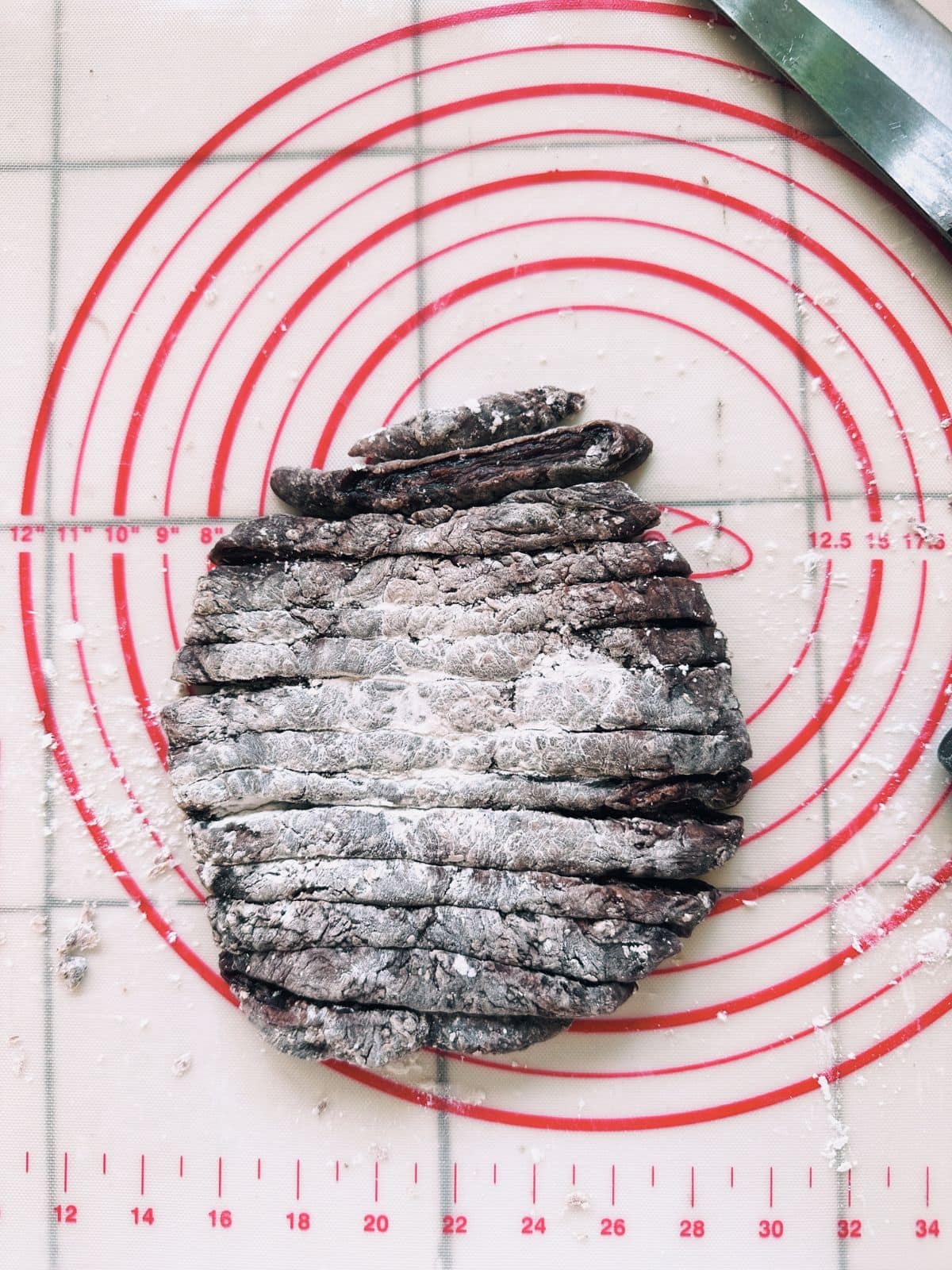 Flattened tapioca dough cut into thin, even strips on a starch-dusted surface.