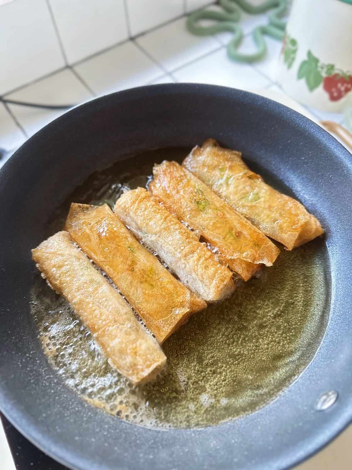 Frühlingsrollen aus Vietnam (Vietnamese Spring Rolls) Vietnamese spring rolls frying in a skillet, sizzling in hot oil until golden and crispy.