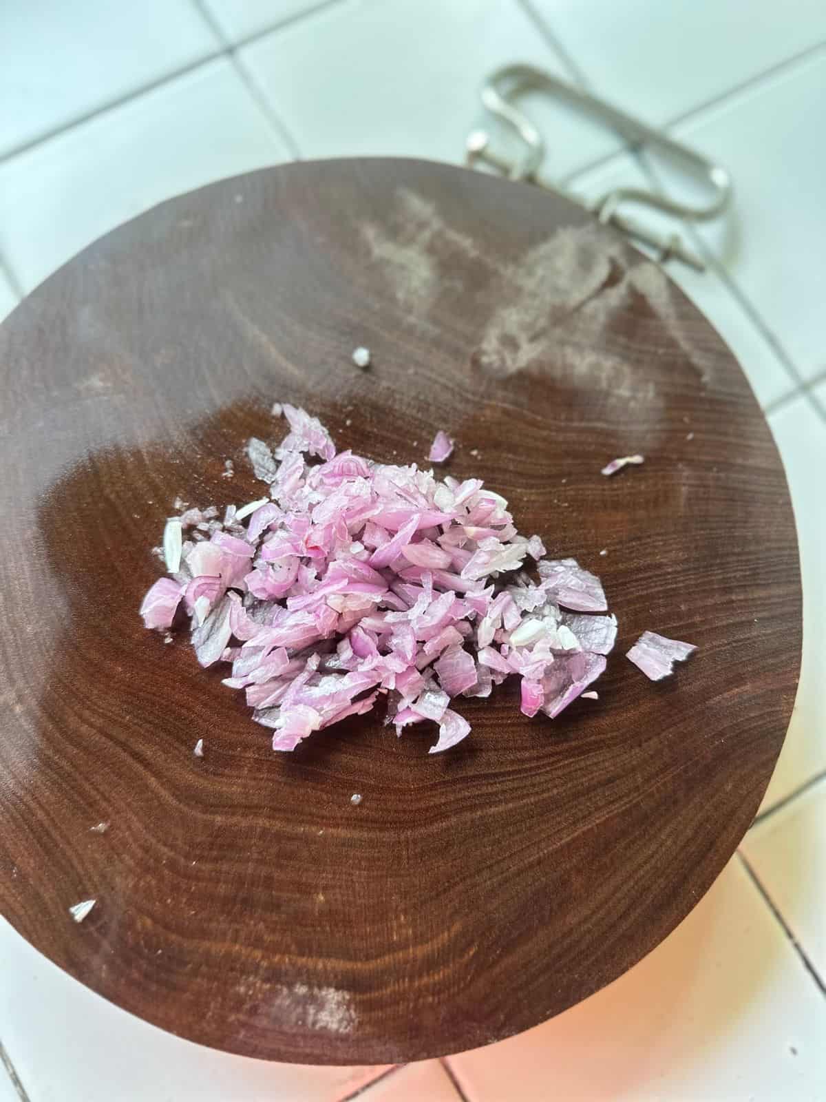 Finely minced shallots on a wooden cutting board, ready for cooking.
