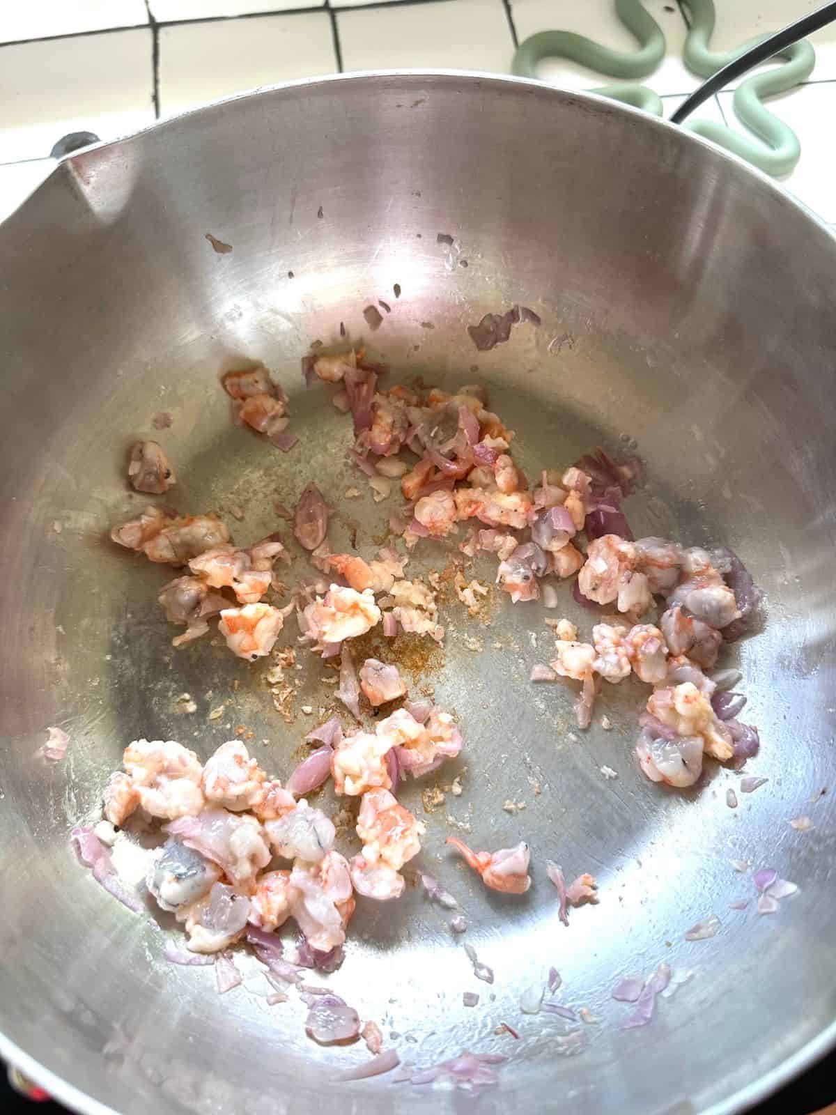 Shallots and shrimp stir-frying in a pot, releasing their aroma before adding water.