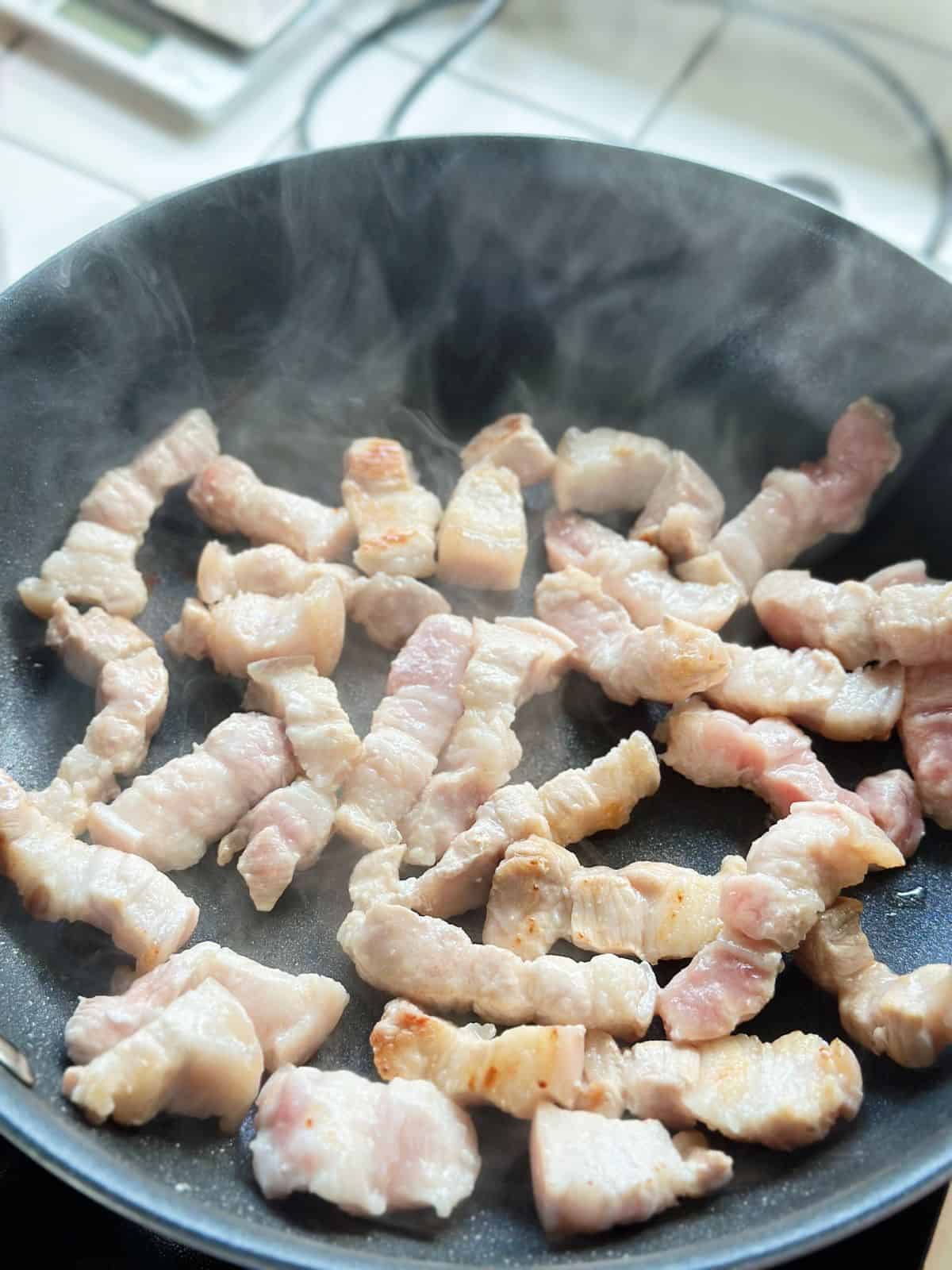 Lightly golden seared pork belly chunks in a skillet, edges turning crispy for Vietnamese caramelized pork belly.