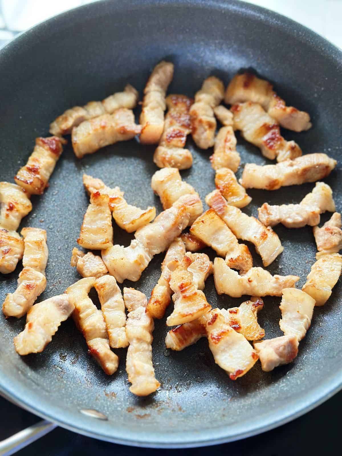 Golden seared pork belly chunks in a skillet, edges turning crispy for Vietnamese caramelized pork belly.