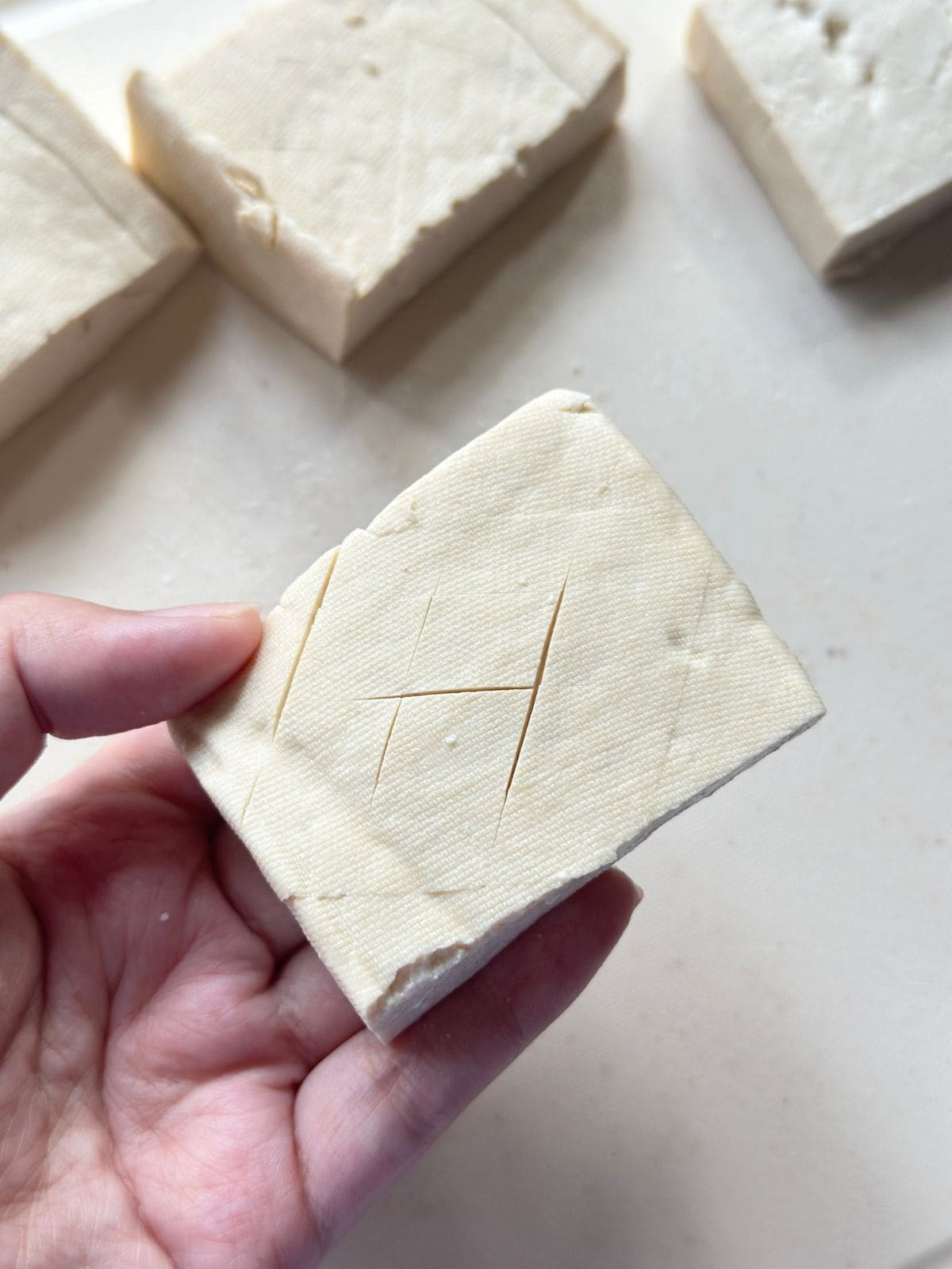 A piece of tofu with light criss-cross cuts on one side.