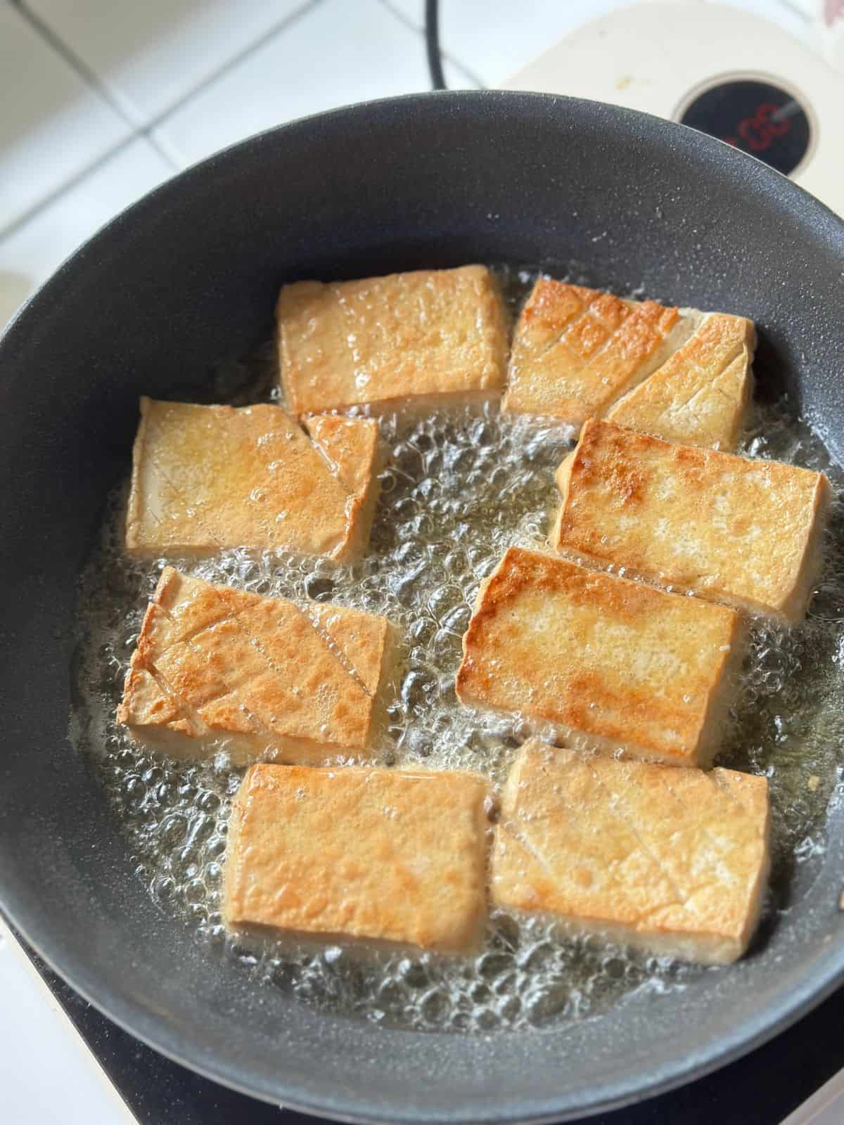 Crispy tofu cubes sizzling in a skillet, turning golden on all sides.