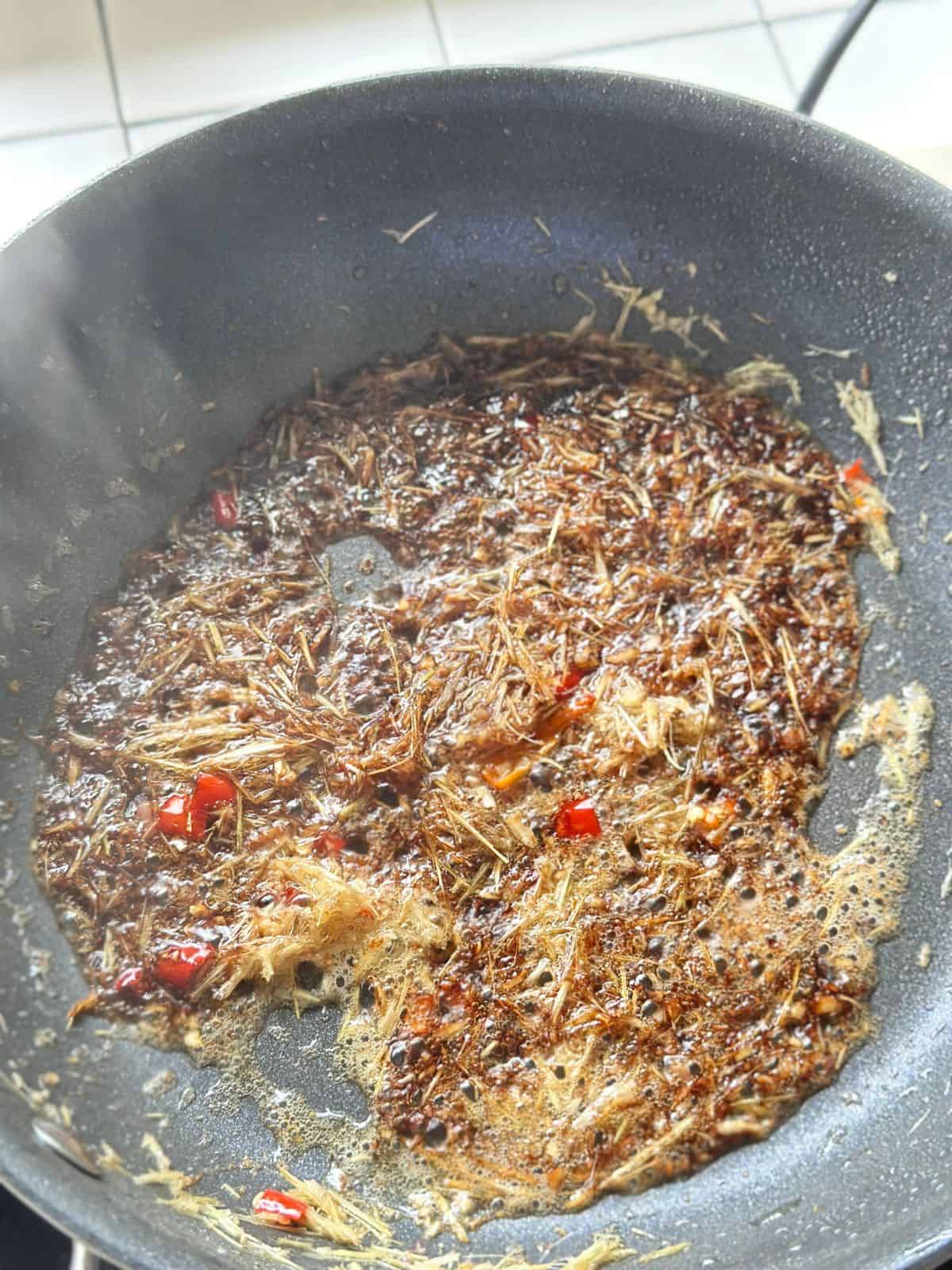 Sauce cooking in a skillet with lemongrass, bubbling gently.
