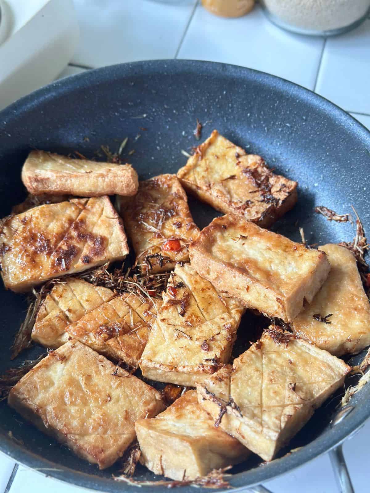 Golden fried tofu pieces coated in flavorful lemongrass sauce, tossed in a skillet.