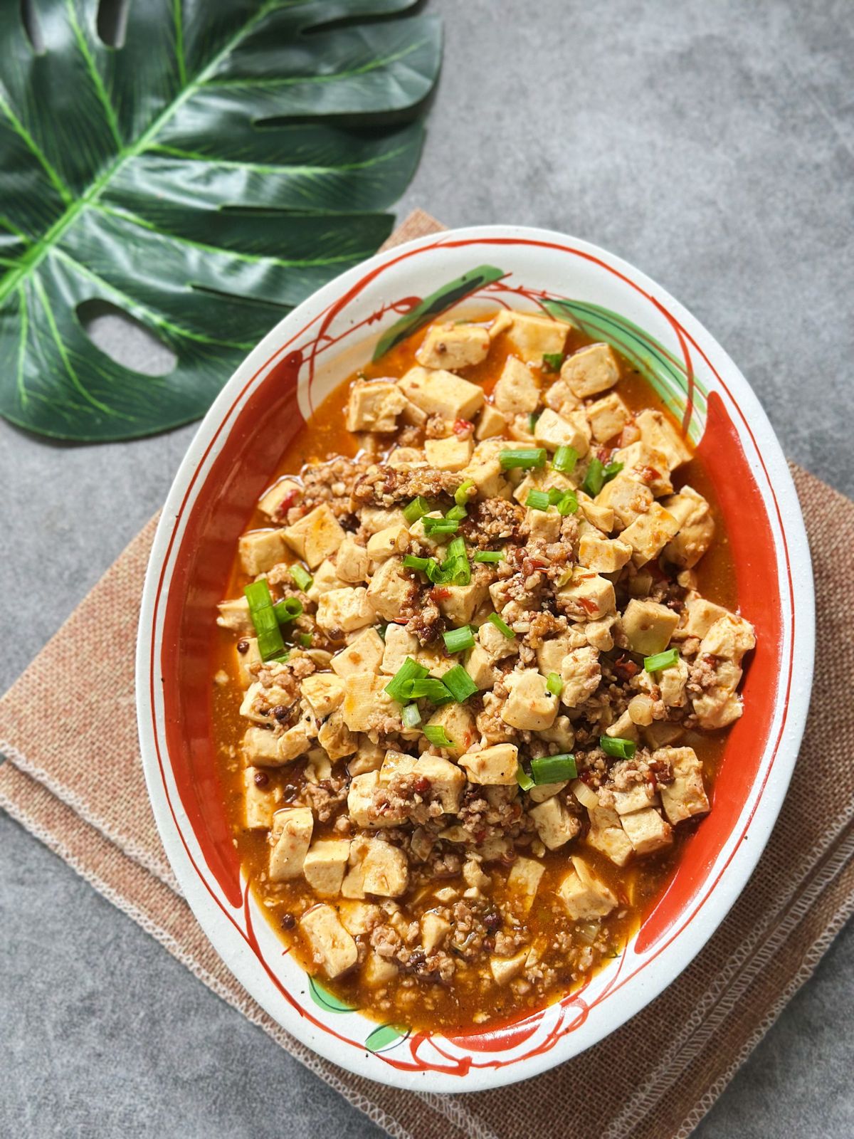 A plate of Mapo Tofu with soft tofu cubes in a bright red Sichuan chili sauce, topped with scallions and ground meat.