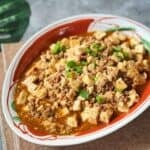 Mapo Tofu served in a shallow bowl, coated in a glossy, spicy doubanjiang sauce with Sichuan pepper flakes.