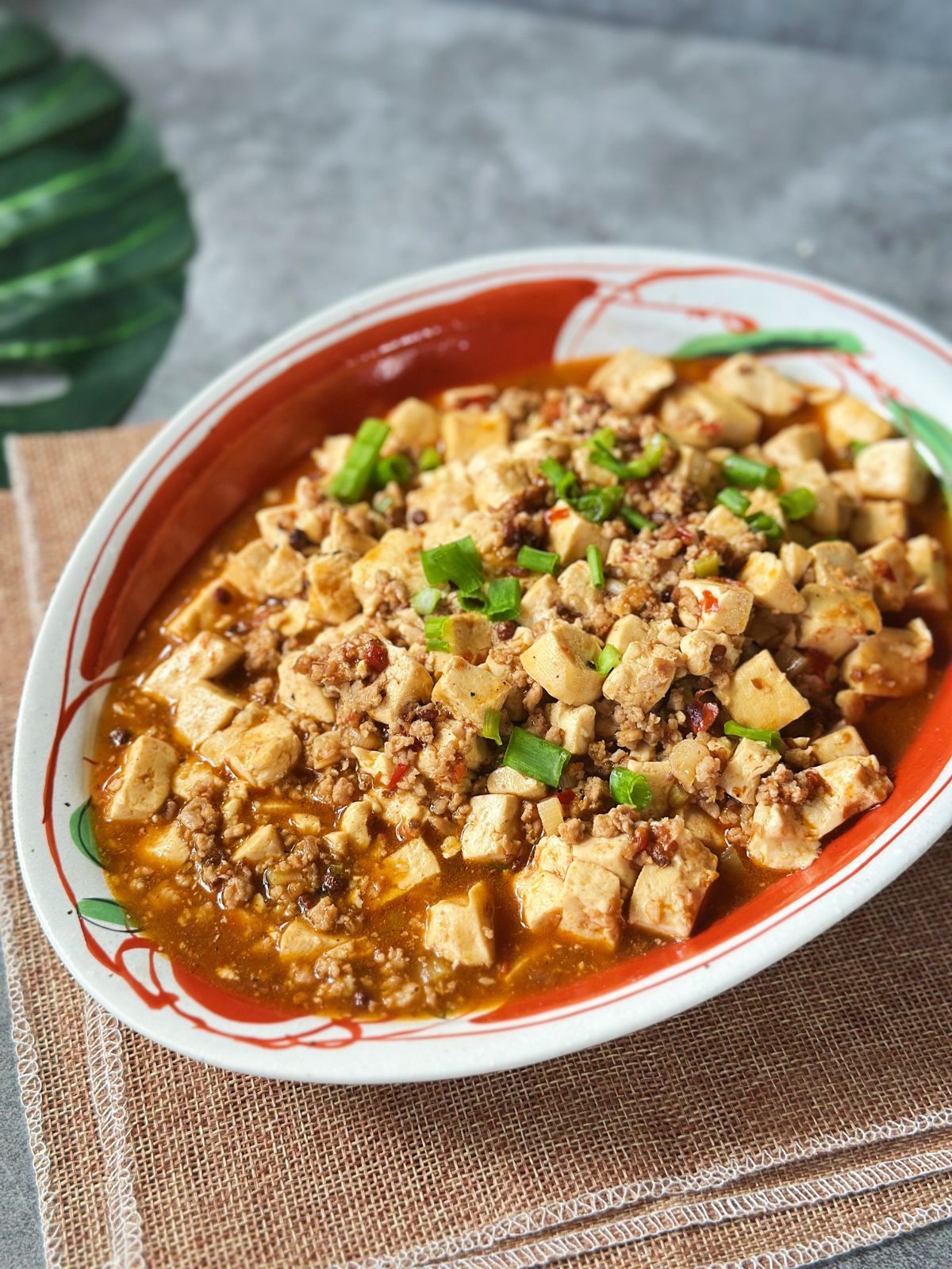 Mapo Tofu served in a shallow bowl, coated in a glossy, spicy doubanjiang sauce with Sichuan pepper flakes.