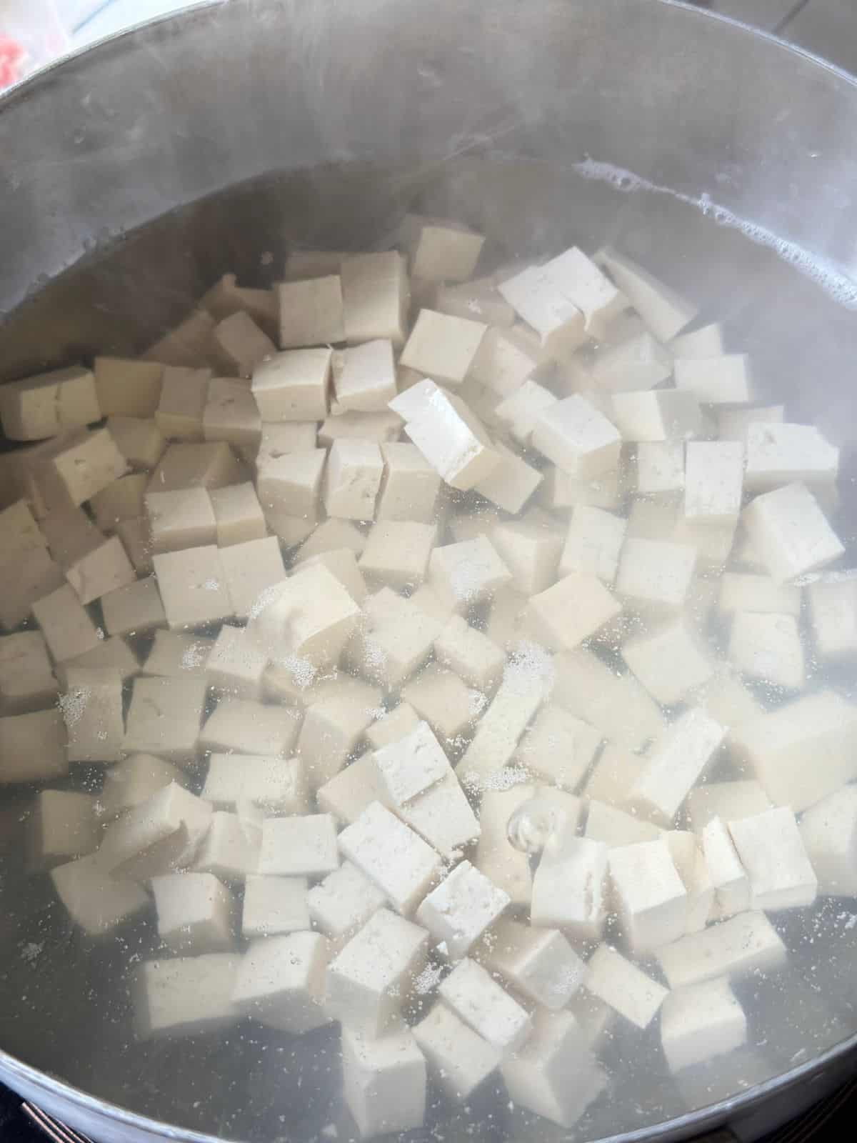 Soft tofu pieces gently boiling in salted water inside a pot.