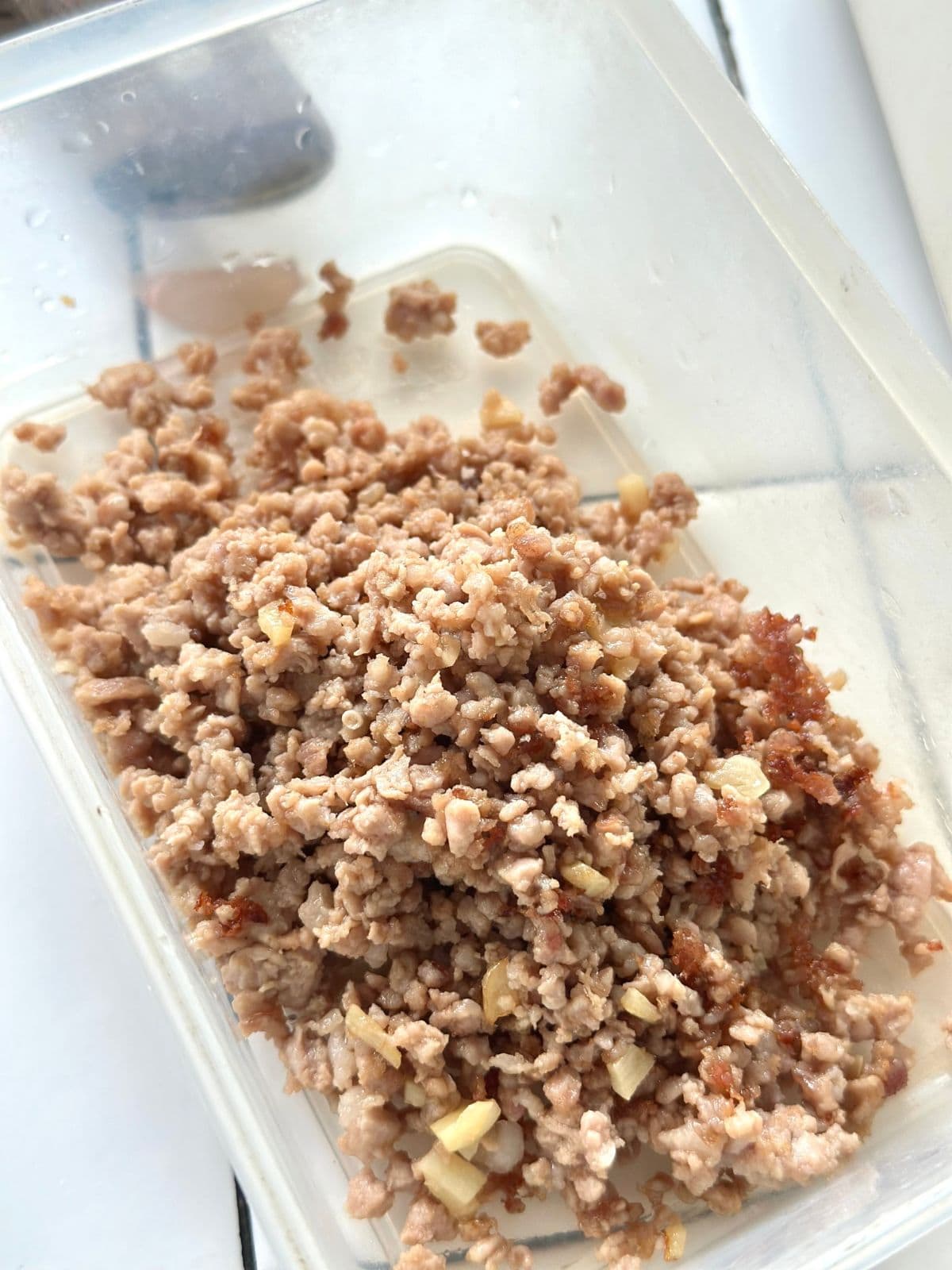 Cooked ground pork spread out in a containter after browning.