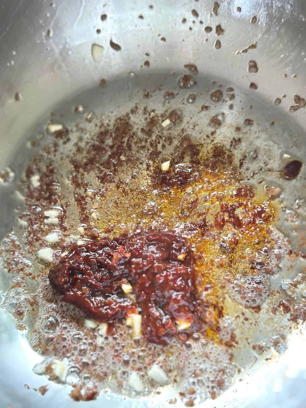Doubanjiang chili bean paste being fried in a pot until the oil turns red.